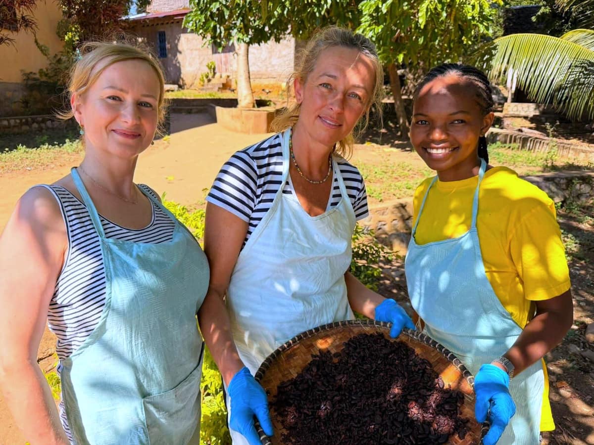 Trois participantes en tablier présentent un van de fèves de cacao
